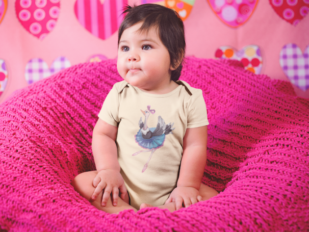 beautiful little baby girl sitting on a pink sofa while wearing a onesie a14047 2