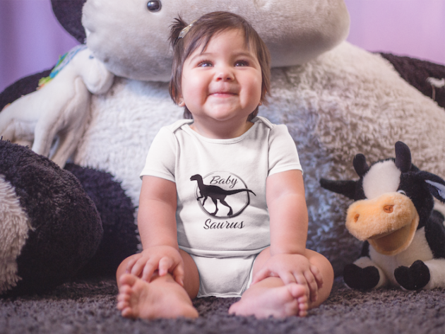mockup of a little baby girl sitting down while smiling and wearing a onesie near her teddy a14045 2 1