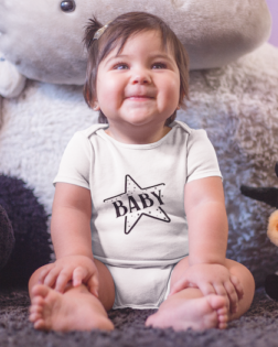 mockup of a little baby girl sitting down while smiling and wearing a onesie near her teddy a14045 2