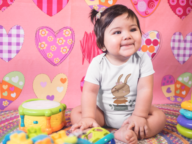 mockup of a very happy baby girl sitting down on her playing room while wearing a onesie a14052 1