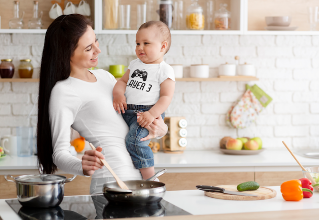 onesie mockup of a mom holding his baby while cooking in her kitchen 34625 r el2 1